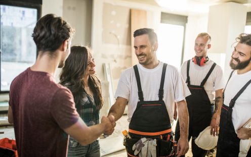 Happy manual worker welcoming young couple to their renovated apartment.