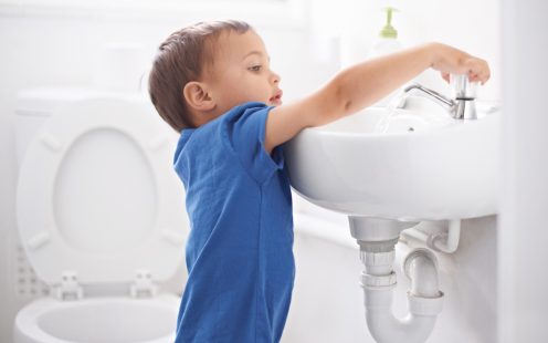 Shot of a cute young boy washing his hands in a bathroom