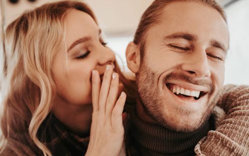 Love is in the air. Close up portrait of happy woman whispering on ear something pleasant to her beloved laughing hipster man while embracing him