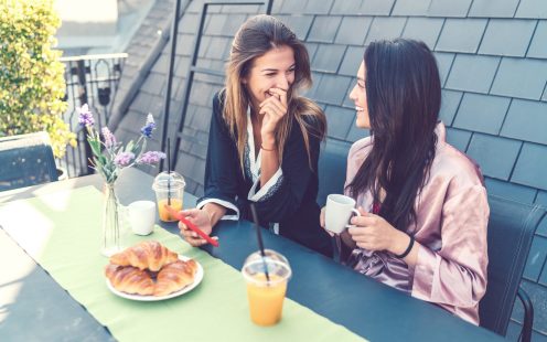 Two women enjoying breakfast at rooftop terrace and using smartphone