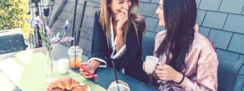 Two women enjoying breakfast at rooftop terrace and using smartphone